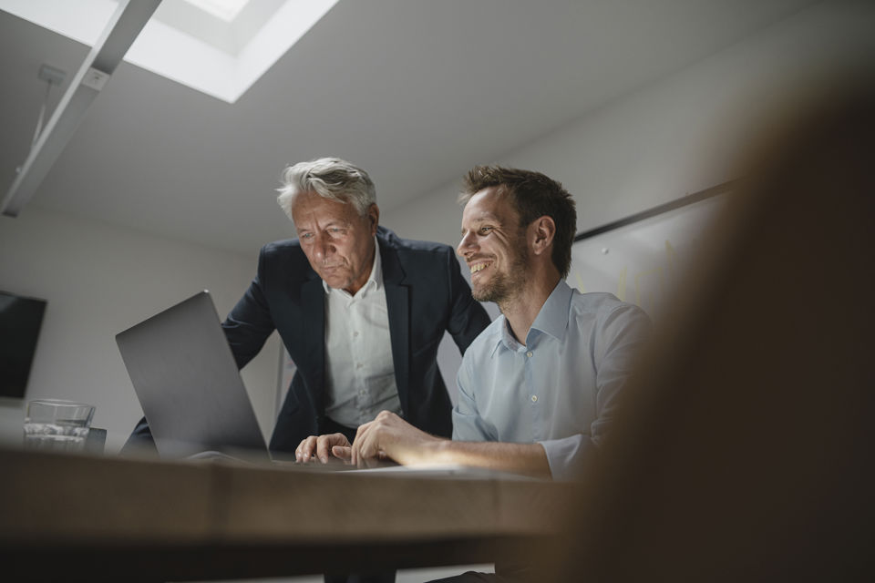 Zwei Männer in einem Besprechungsraum schauen auf den Bildschirm eines Laptops
