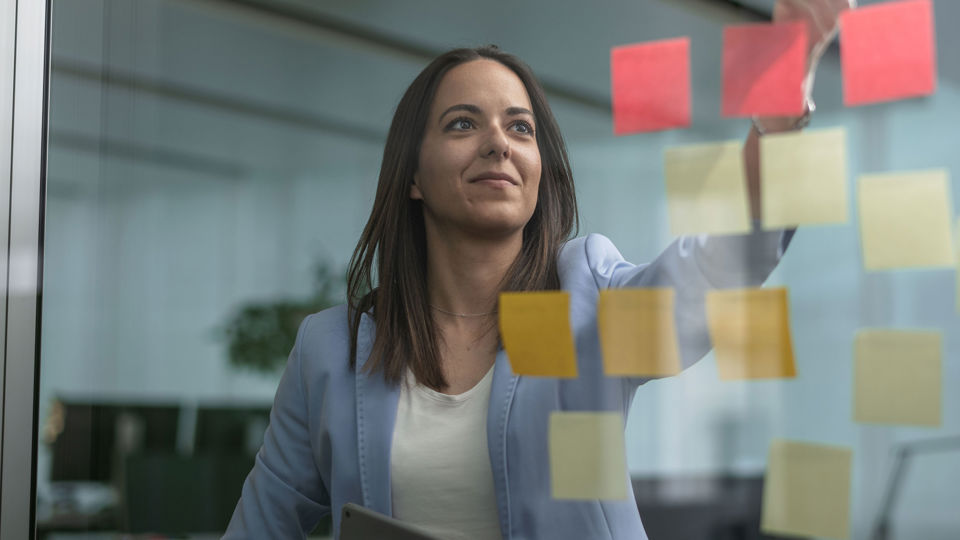 Eine Frau klebt bunte Post-it Zettel an eine Glaswand