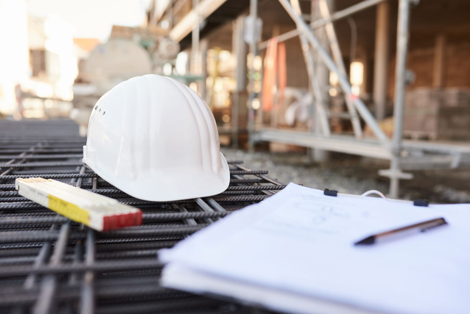 Bauhelm, Notizzettel und Messband liegen auf einer Baustelle