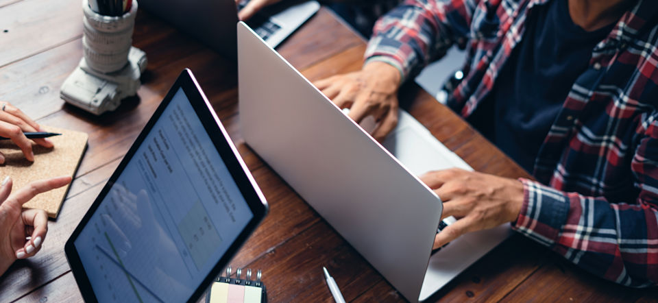 Zwei Personen arbeiten an einem Tisch mit Laptop und Tablet