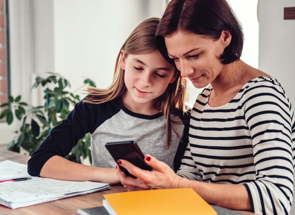 Eine Mutter hilft ihrer Tochter bei den Hausaufgaben und beide schauen auf ein Smartphone 