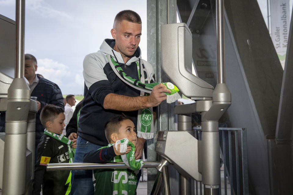 Foto eines Vaters mit seinem kleinen Sohn, die an einem Drehkreuz den FC St.Gallen Fanschal mit eingenähtem Chip verwenden, um ins Stadion zu kommen.