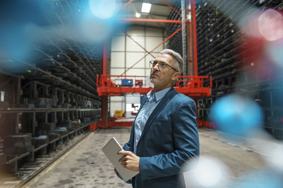 Ein Mann in einem Business-Anzug steht in einer grossen Lagerhalle und schaut die Bestände an