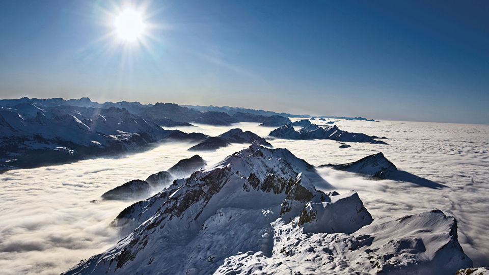 Blick von einem hohen Berggipfel auf Bergspitzen, die aus den Wolken ragen